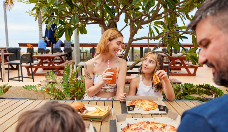 Parent and Child eating pizza and drinking, smiling at each other.