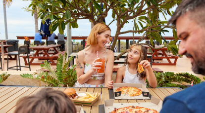 Parent and child smiling, eating pizza and drinking