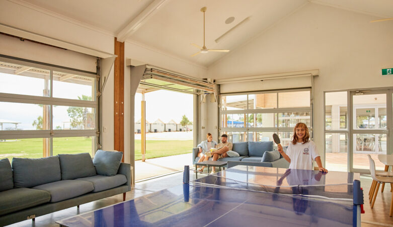 Child playing table tennis whilst parents sit on couch reading in recreation room