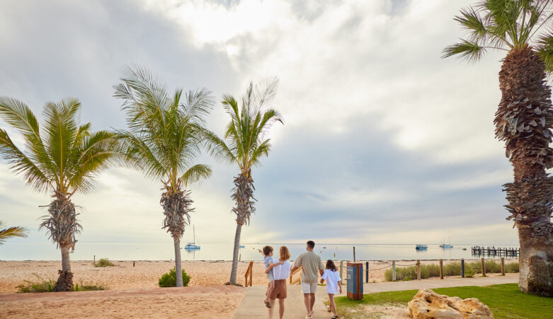 Family of four walking along path towards palm lined beach