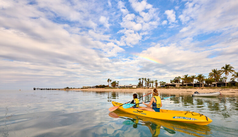 Parent and child on kayak, paddling near tropical beach