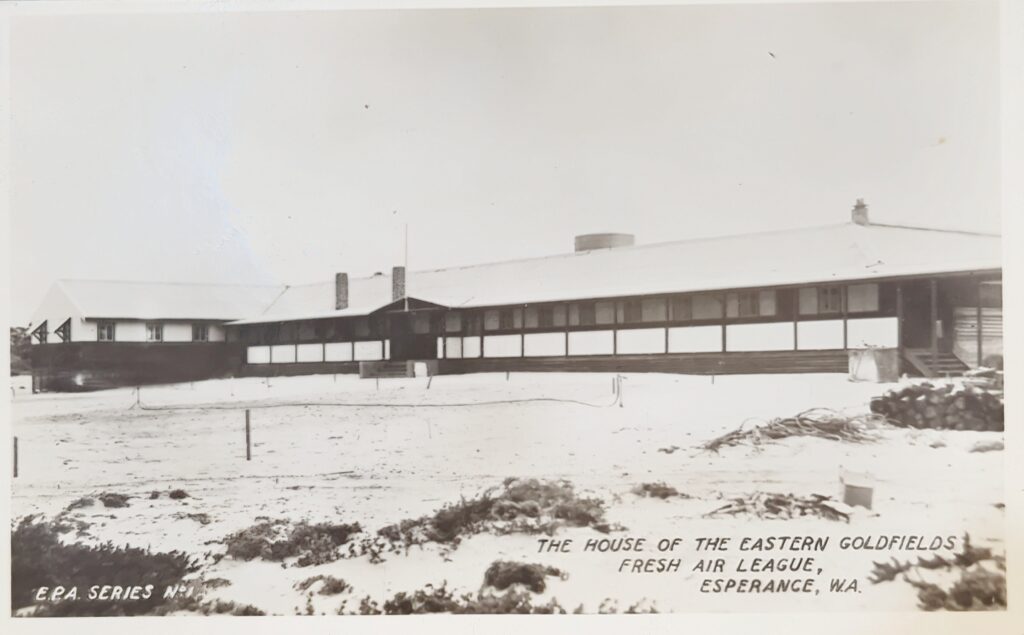 Old, faded image of the original fresh air league building, surrounded by sand.