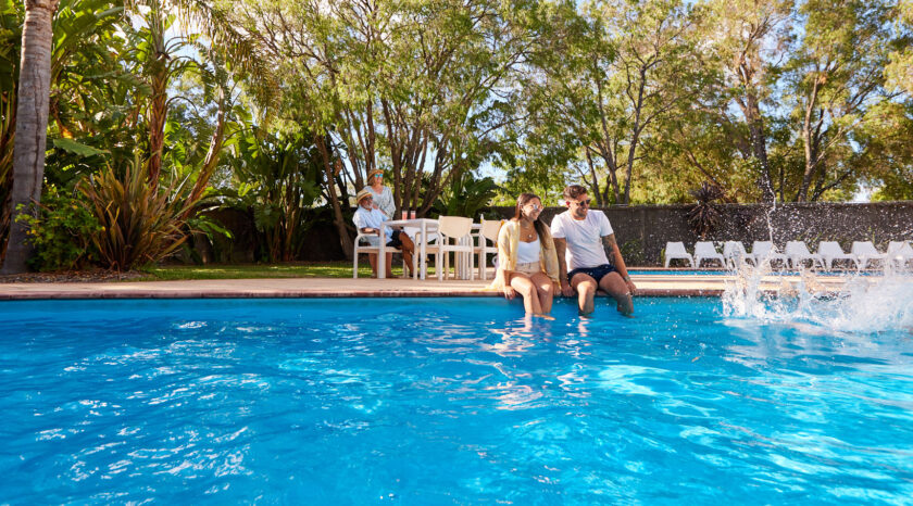 Parents and grandparents sit at pool's edge as children jump into the water