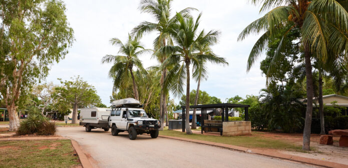 4WD car pulling campertrailer driving through caravan park with tropical palm trees