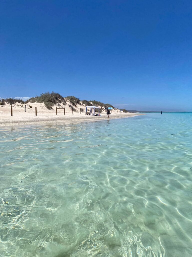 Clear blue waters and white sand dunes in background