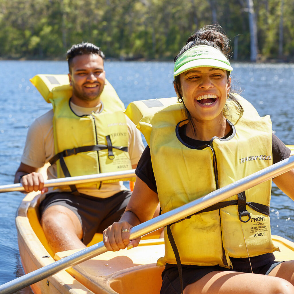 A couple wearing yellow lifejackets kayak on the lake in Karri Valley