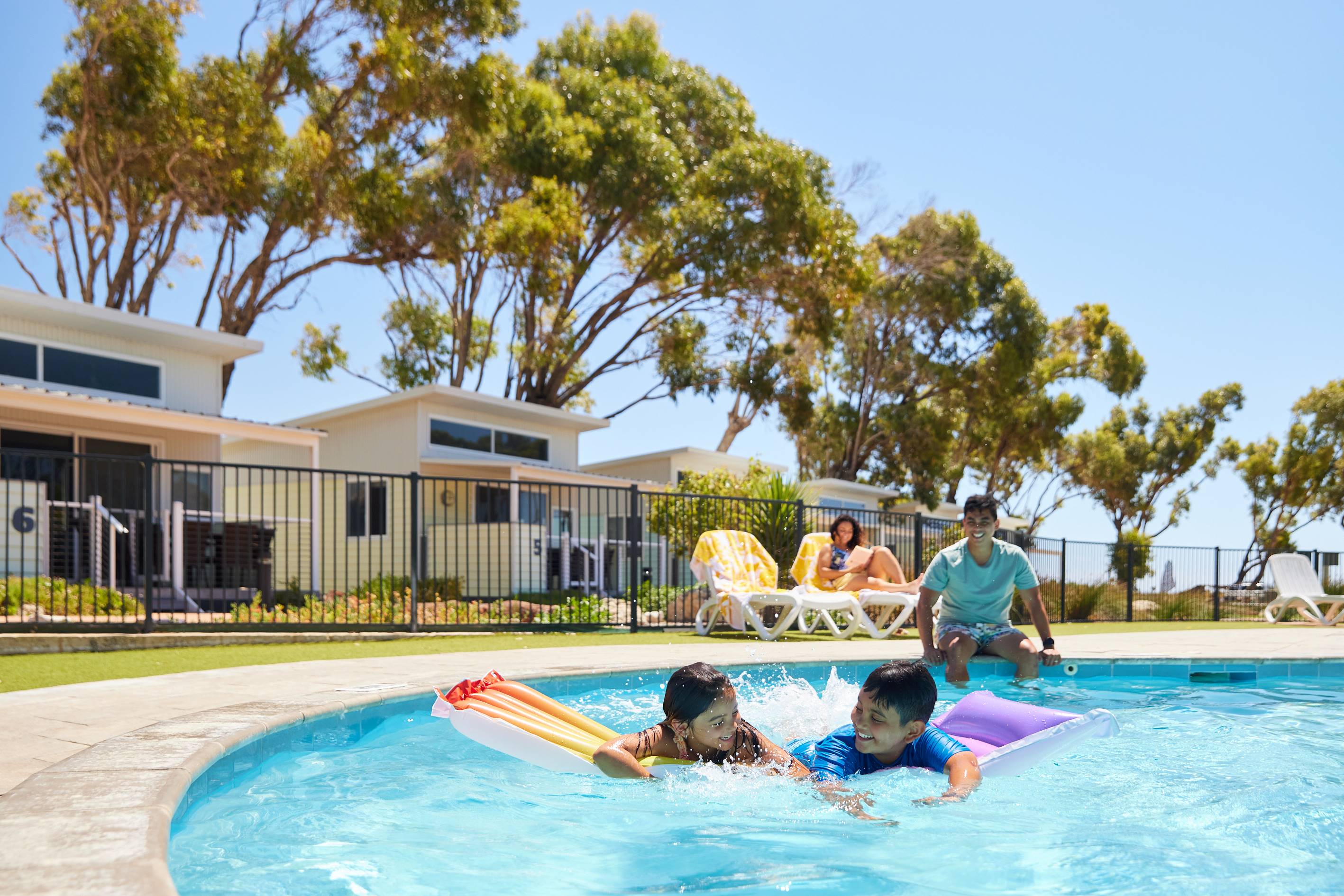 Family making a splash in the pool, with parents supervising from the pool lounge and edge.