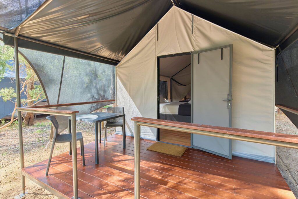 Modern Safari Exterior featuring a wooden deck with a table and chairs. The tent's open door revealing the interior space. 