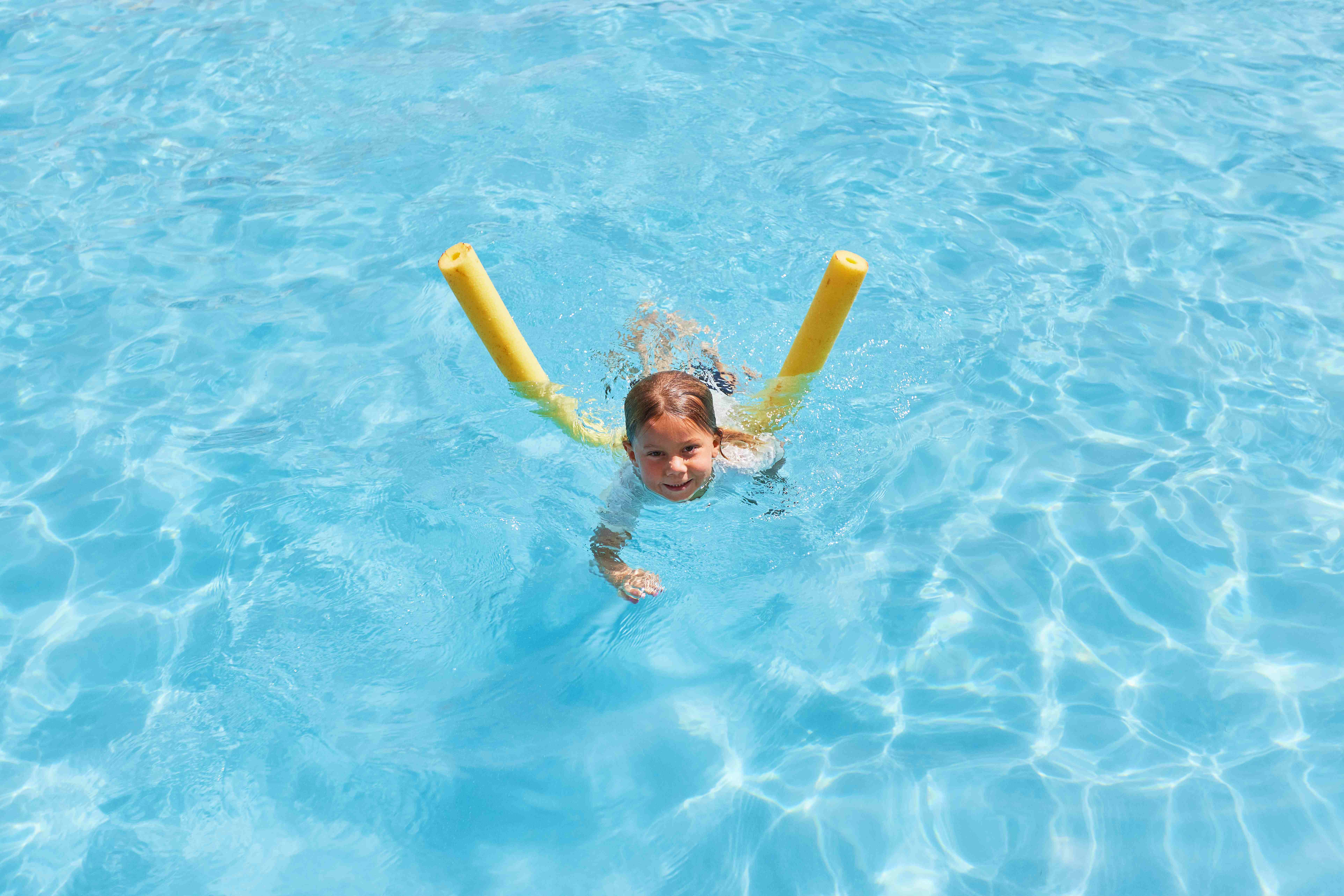 A child swimming with a yellow pool noodle in the crystal-clear water.