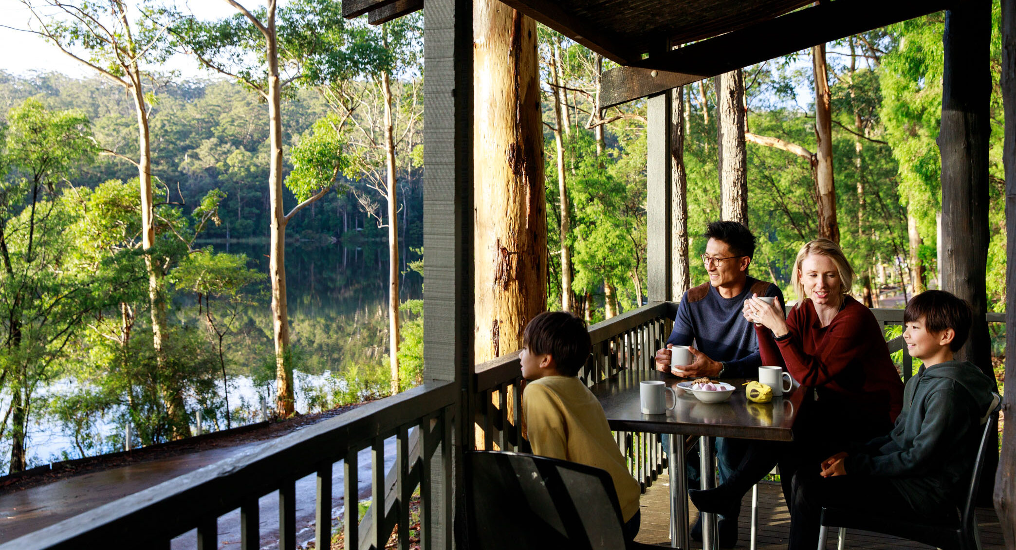 Family enjoying a hot drink on the balcony of a RAC Karri Valley Resort chalet.